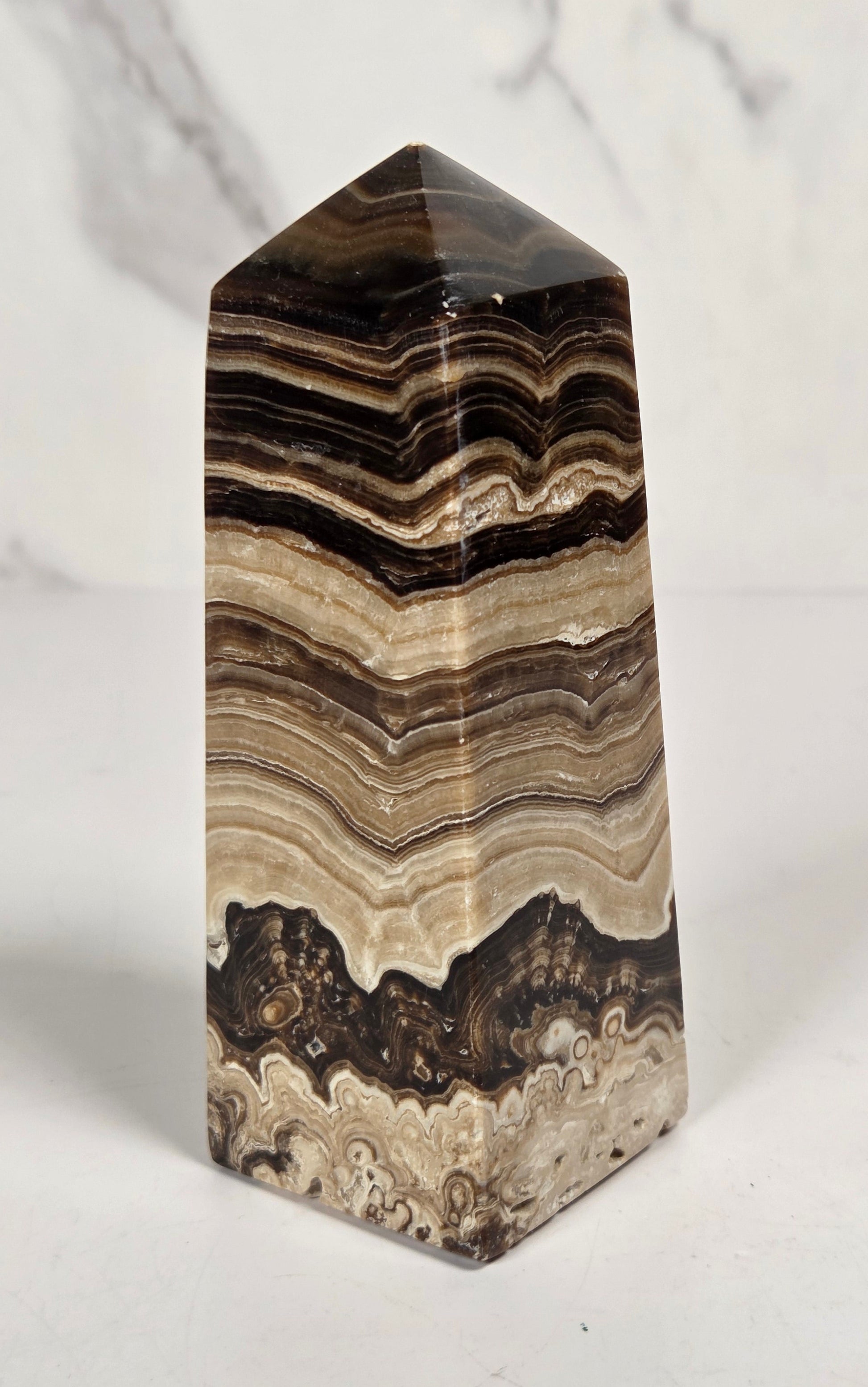 Banded chocolate calcite tower with brown and tan coloring on a white background