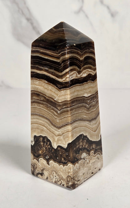 Banded chocolate calcite tower with brown and tan coloring on a white background