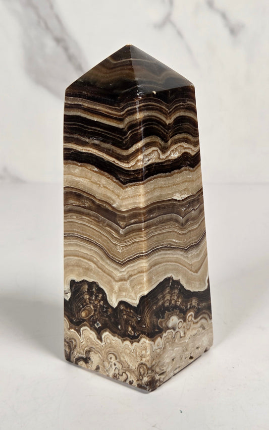 Banded chocolate calcite tower with brown and tan coloring on a white background