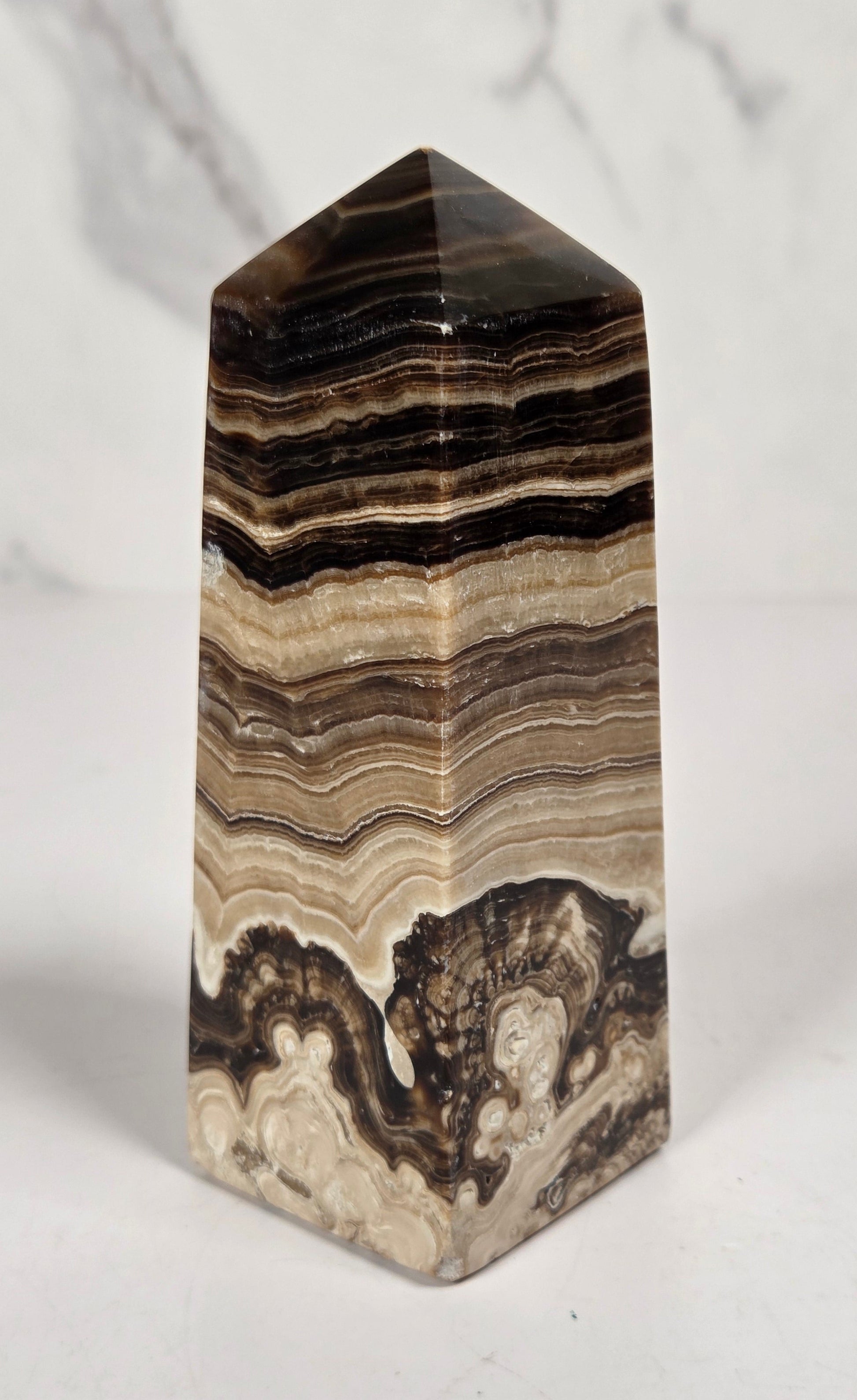Banded chocolate calcite tower with brown and tan coloring on a white background