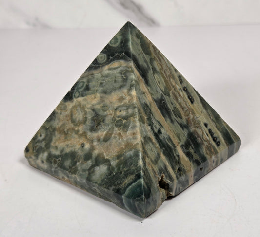 Pyramid shaped crystal with green and yellow coloring and orbicular patterns, on a white background