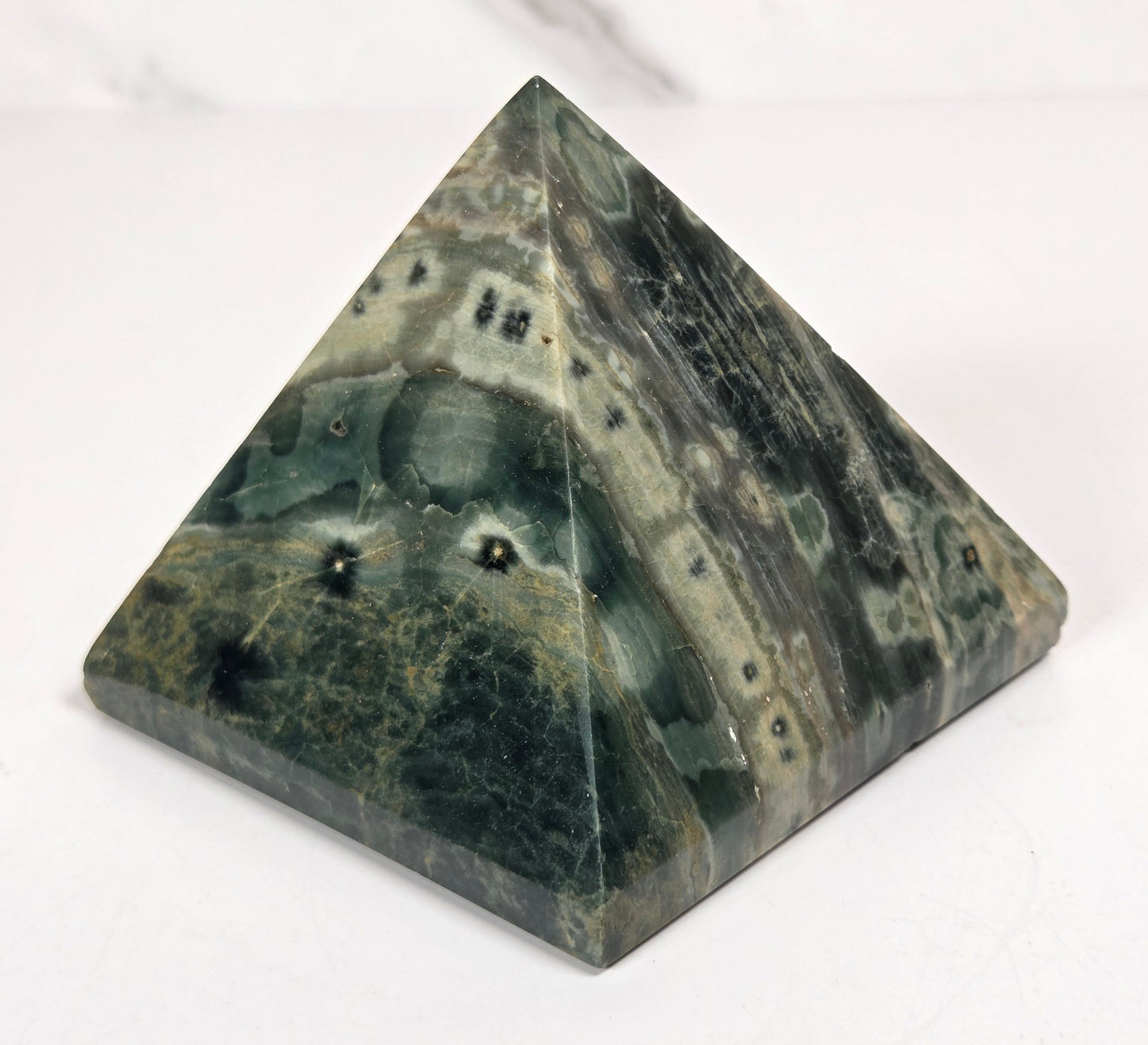 Pyramid shaped crystal with green and yellow coloring and orbicular patterns, on a white background