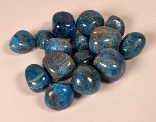 A group of polished blue tumbled gemstones,blue apatite, arranged on a plain light beige background.