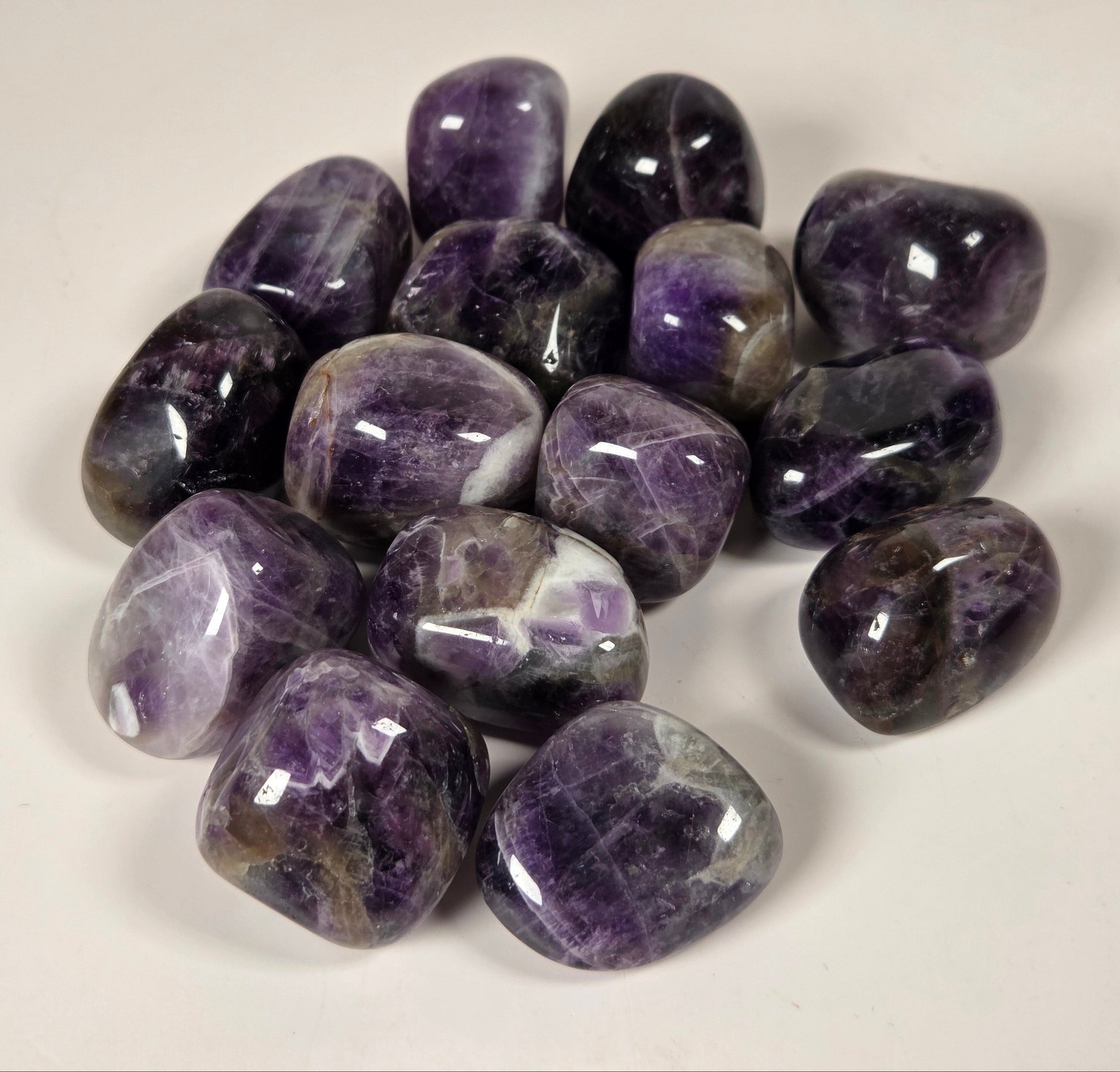 A pile of polished purple amethyst tumbled stones on a plain off-white background.