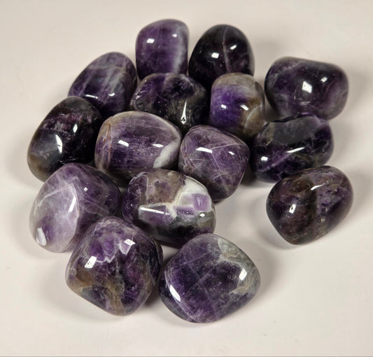 A pile of polished purple amethyst tumbled stones on a plain off-white background.