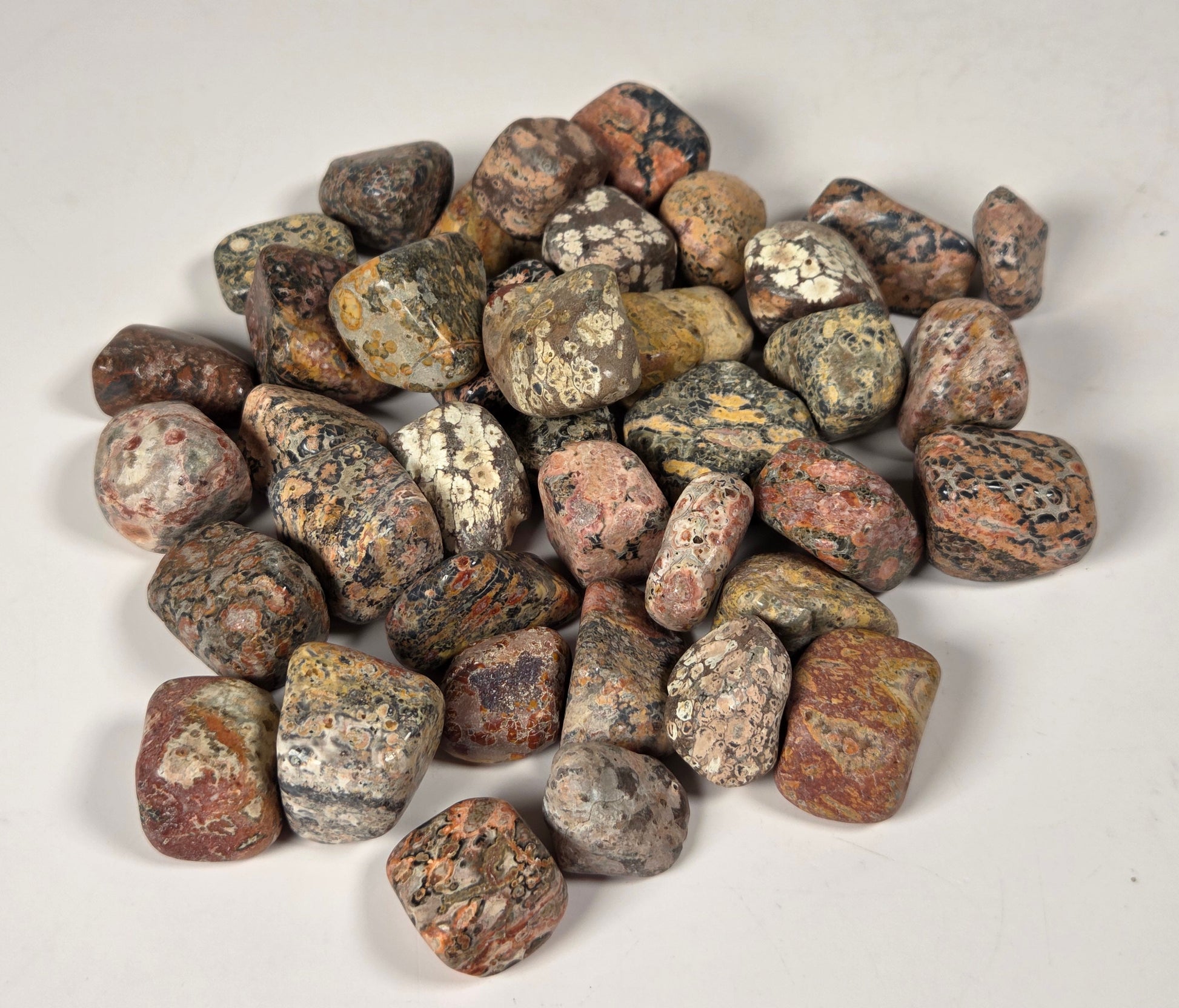 A pile of small polished river stones or pebbles in mixed earthy colors, including brown, gray, beige, and reddish tones, photographed on a plain light background.