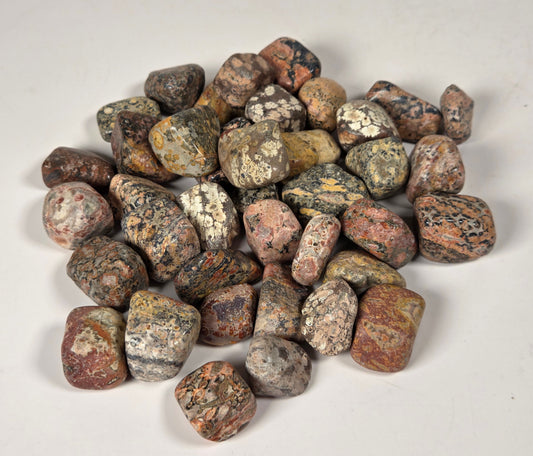 A pile of small polished river stones or pebbles in mixed earthy colors, including brown, gray, beige, and reddish tones, photographed on a plain light background.