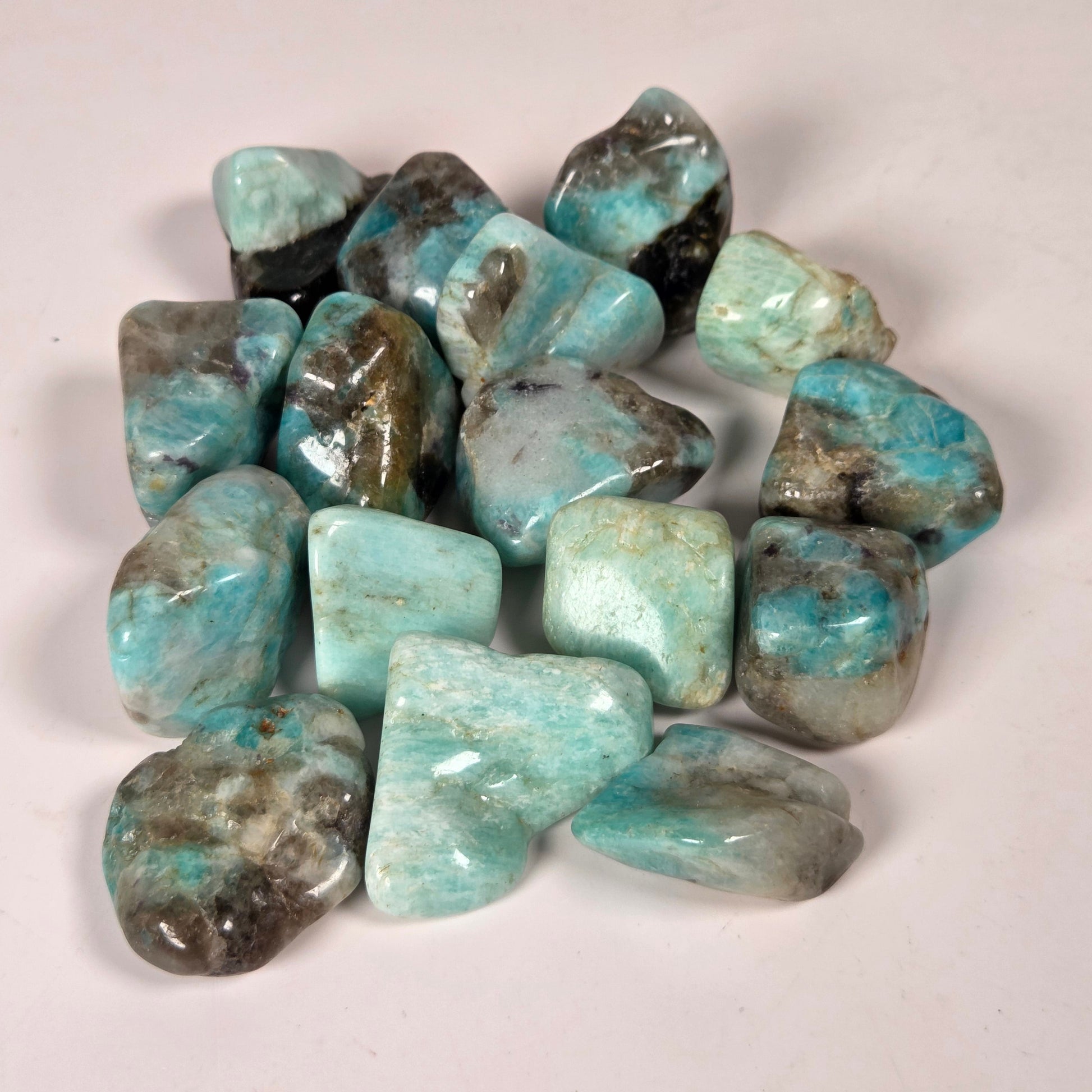 A pile of polished tumbled stones in light blue, turquoise, gray, and dark brown/black marbled patterns, arranged on a plain off-white background.