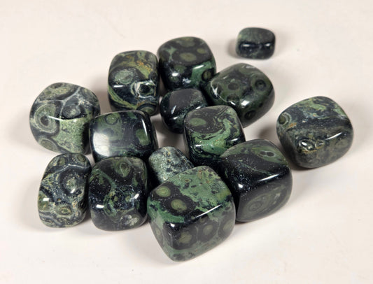A group of polished dark green and black mottled stone tumbled cubes, arranged on a plain off-white background.