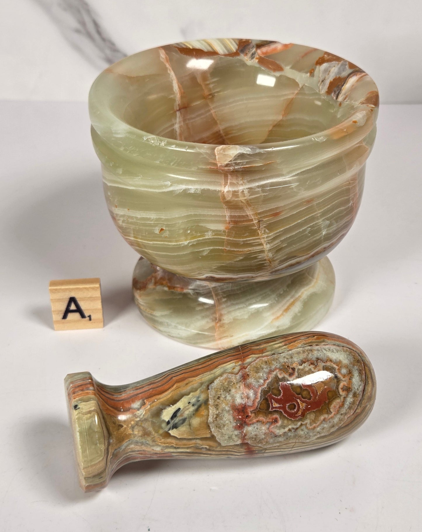 A carved stone goblet and matching stone stopper, both featuring natural agate-like banding in beige, brown, and cream tones, displayed on a light gray surface.
