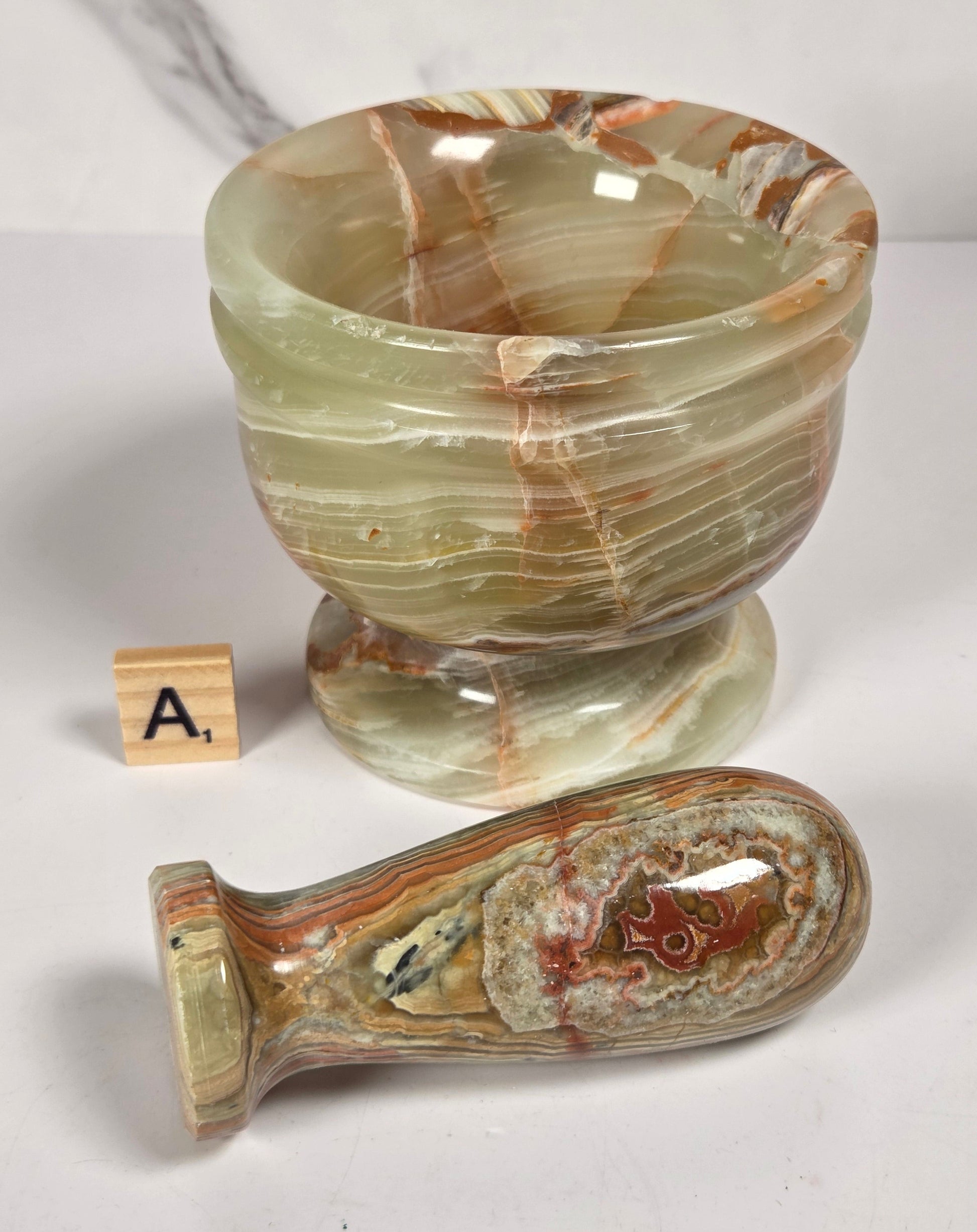A carved stone goblet and matching stone stopper, both featuring natural agate-like banding in beige, brown, and cream tones, displayed on a light gray surface.