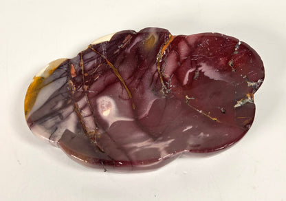 A polished decorative stone dish with organic, irregular shapes, featuring a marbled pattern of deep burgundy, purple, brown, and white with thin gold veins, set against a plain off-white background.