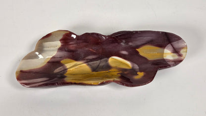 A handcrafted glass dish with an organic, cloud-like silhouette, featuring a marbled pattern of deep burgundy, translucent cream, and ochre yellow on a neutral light gray background.
