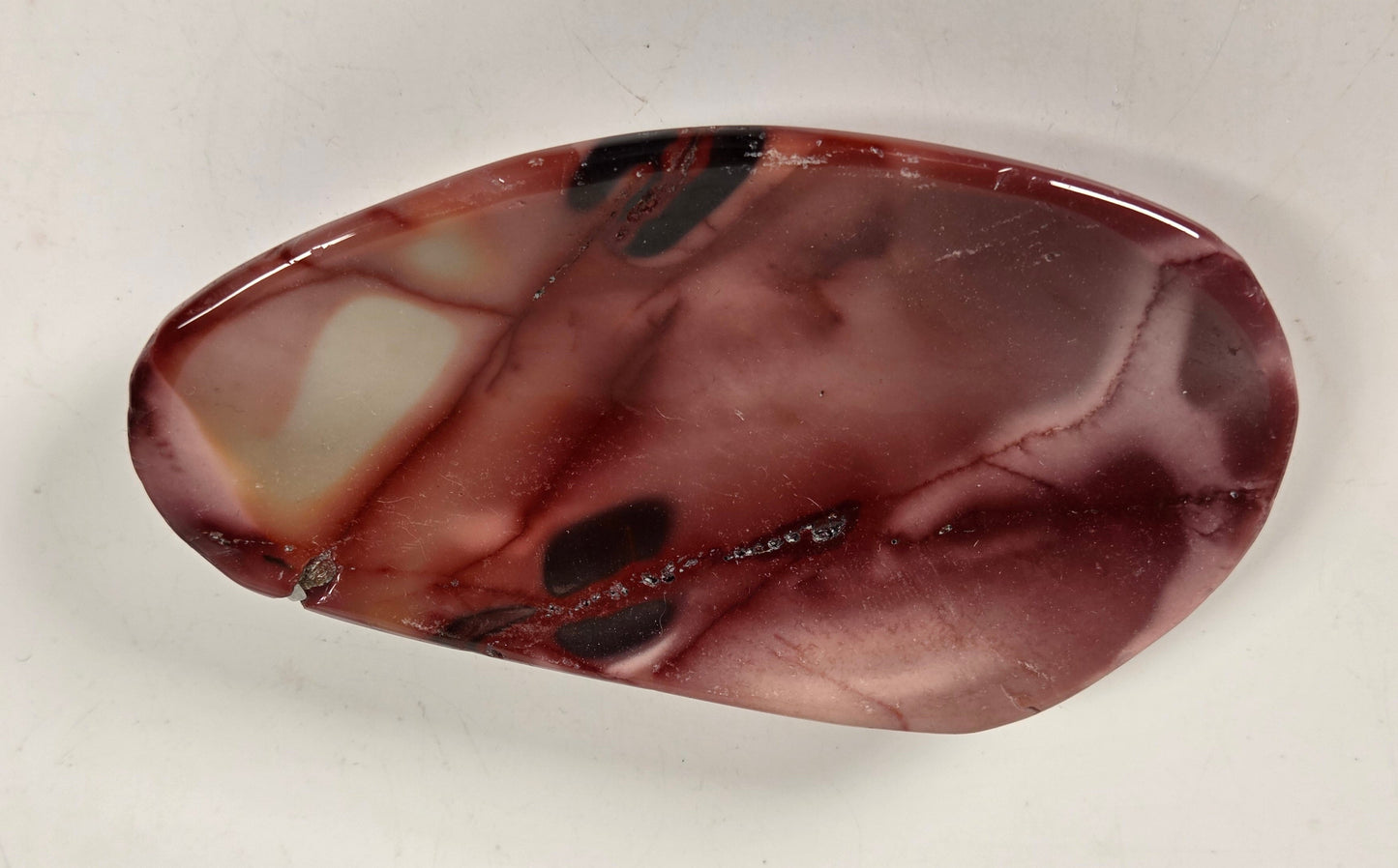 A polished organic-shaped stone cabochon with a marbled pattern of reddish-brown, burgundy, and cream, displayed on a plain off-white background.