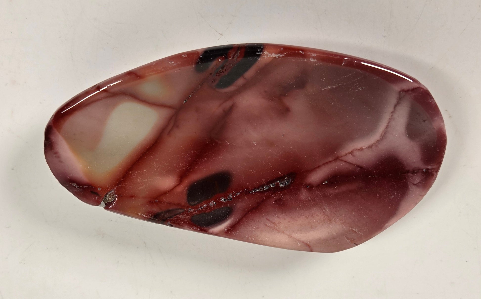 A polished organic-shaped stone cabochon with a marbled pattern of reddish-brown, burgundy, and cream, displayed on a plain off-white background.