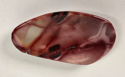 A polished organic-shaped stone cabochon with a marbled pattern of reddish-brown, burgundy, and cream, displayed on a plain off-white background.