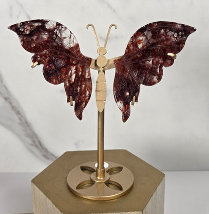 fire quartz carved butterfly wings on a golden staind on a wooden stand againsta a marbled background