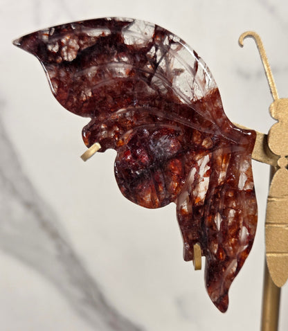 A close-up of a decorative amber-brown leaf-shaped object mounted on a gold-toned display stand against a light marble-like background.
