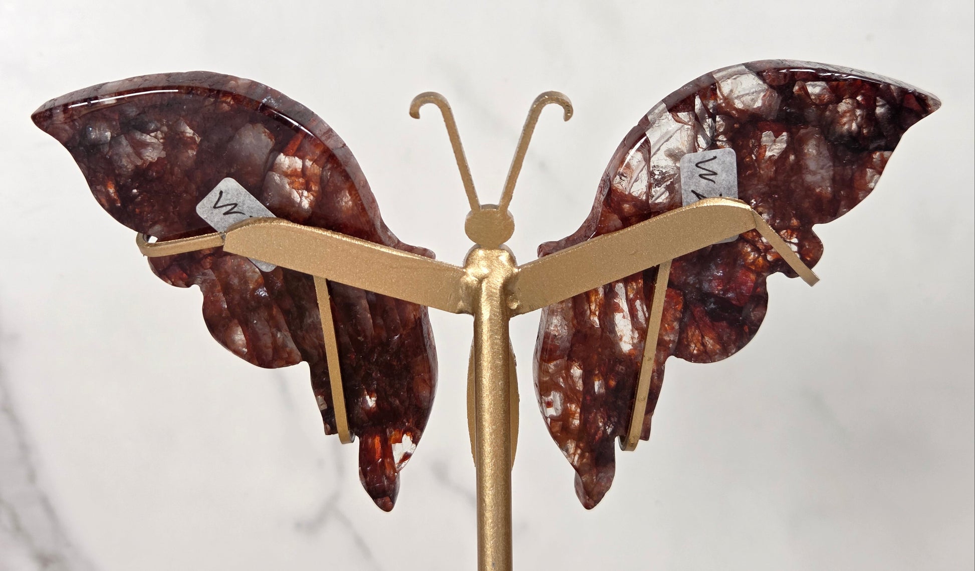 A butterfly-shaped decorative piece with gold-tone metal arms and two marbled brown wings with white inclusions, photographed against a light marble-like background.