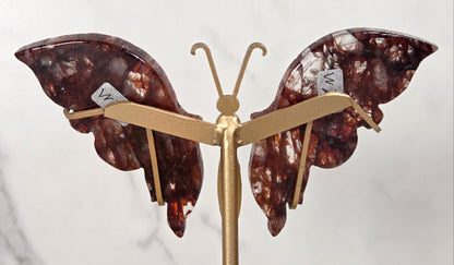 A butterfly-shaped decorative piece with gold-tone metal arms and two marbled brown wings with white inclusions, photographed against a light marble-like background.