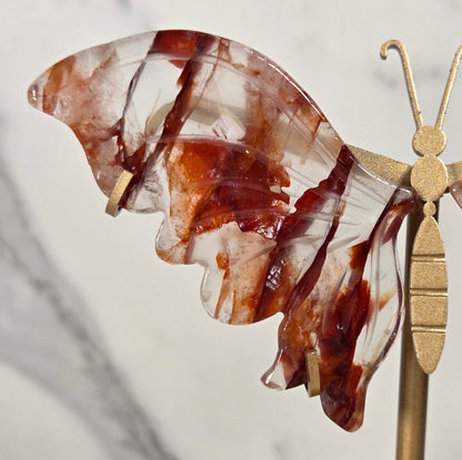 A close-up of a decorative butterfly wall hanging with translucent brown and white marbled wings attached to a gold-toned metal rod mounted on a wall.
