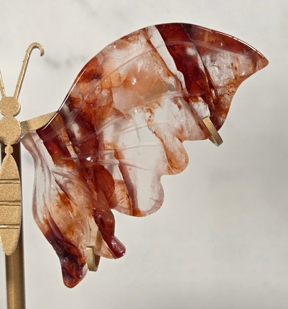 A butterfly-shaped hair claw clip made of marbled amber-brown and translucent resin, attached to a gold-toned metal bar for display.