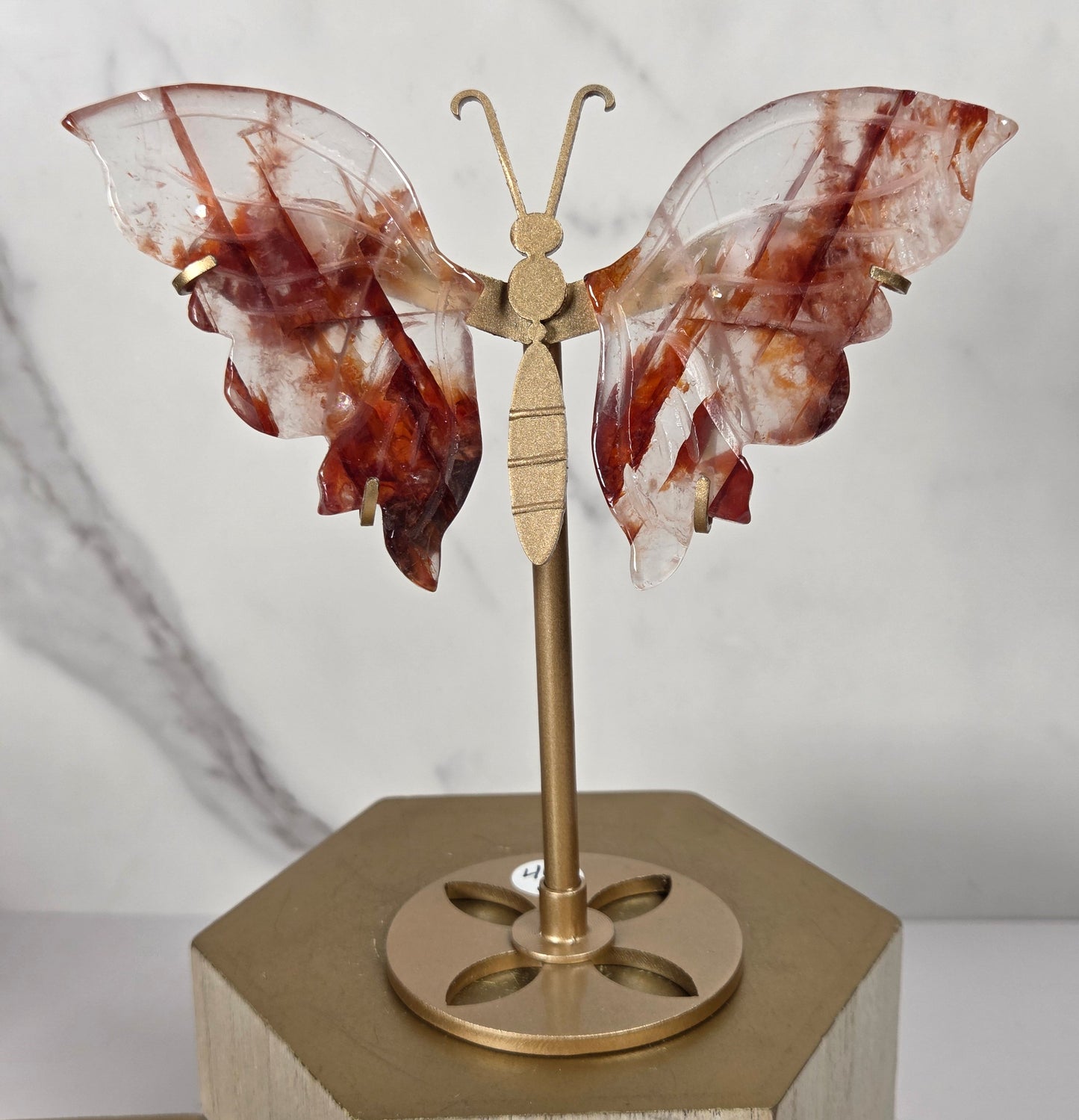 A decorative butterfly wall hanging made from translucent reddish-brown and clear stone wings mounted on a brass rod, attached to a hexagonal light wood block.