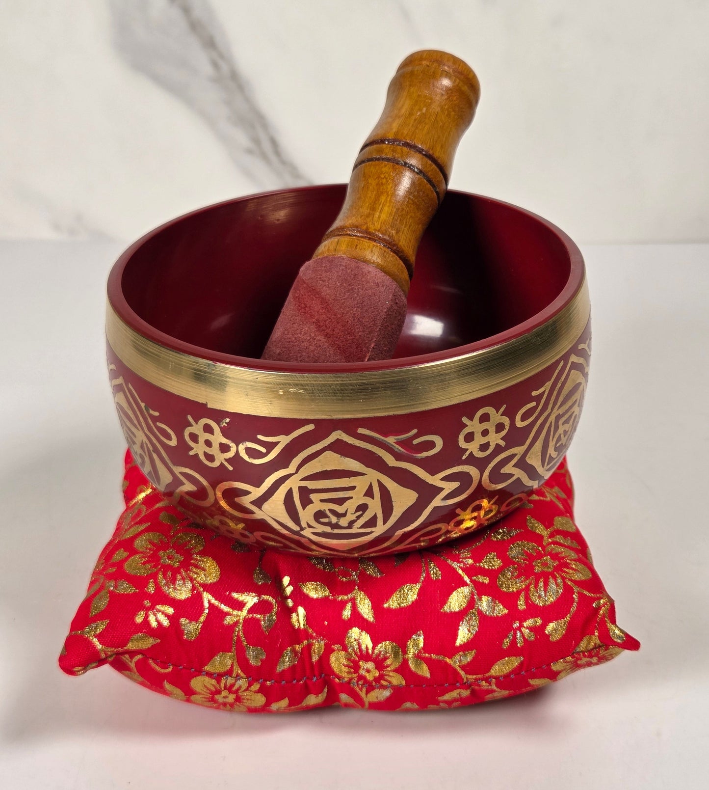 A Tibetan singing bowl in red with a floral pattern on the rim with a cushion and a striker.