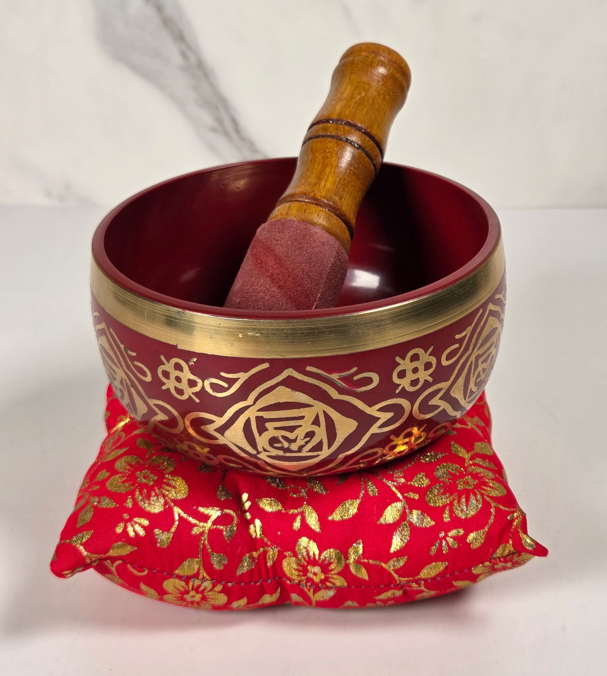 A Tibetan singing bowl in red with a floral pattern on the rim with a cushion and a striker.