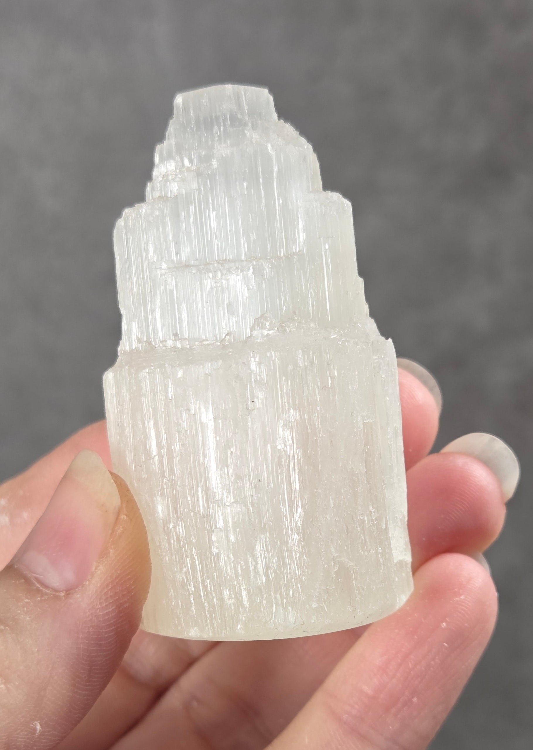 A hand holding a small, layered, translucent white crystal tower against a textured gray background.