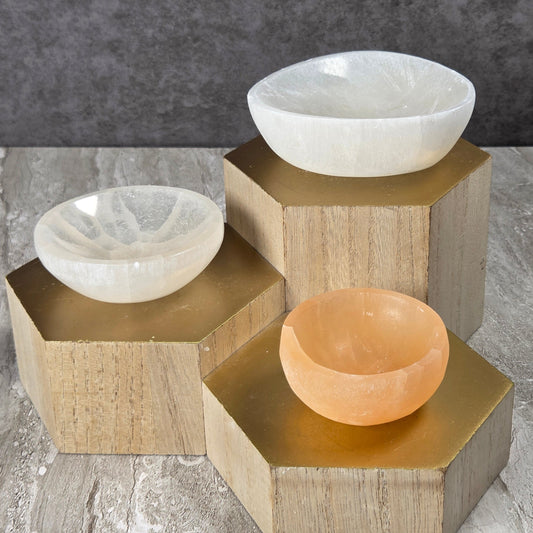 Three crystal bowls mounted on a geometric wooden wall holder against a split gray textured background.