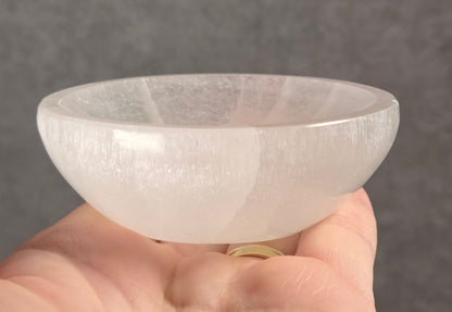 A hand holding a clear, dome-shaped crystal bowl with a textured, frosted surface against a dark gray background.