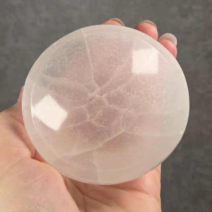 A hand holding a smooth, translucent white crystal sphere with natural internal veining, set against a dark gray textured background.
