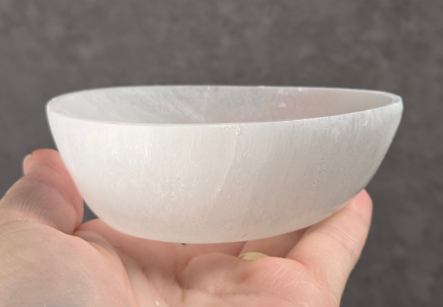 A hand holding a translucent white ceramic or glass bowl against a dark gray textured background.