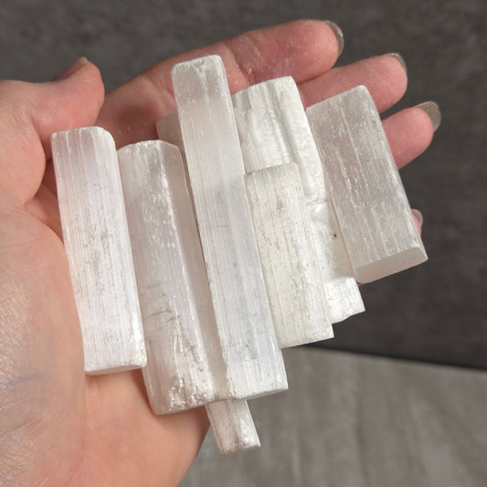 A hand holding a cluster of white selenite crystal sticks against a gray textured background.