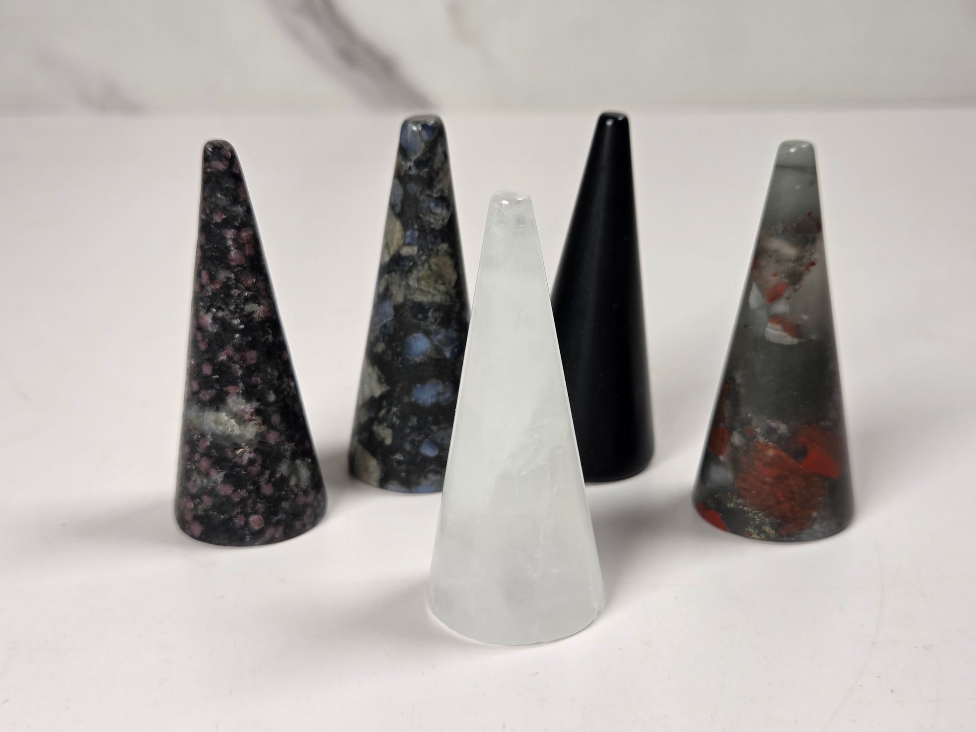 Five pointed crystal cone pendants in various colors and patterns, including black, gray, white, and marbled stone, arranged on a light surface.