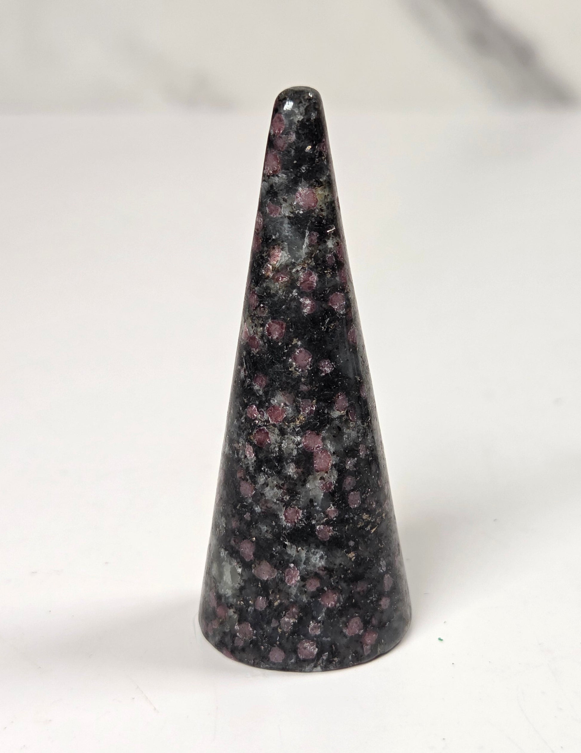 A polished black crystal cone with pinkish-purple and gray flecks, standing upright on a white surface.