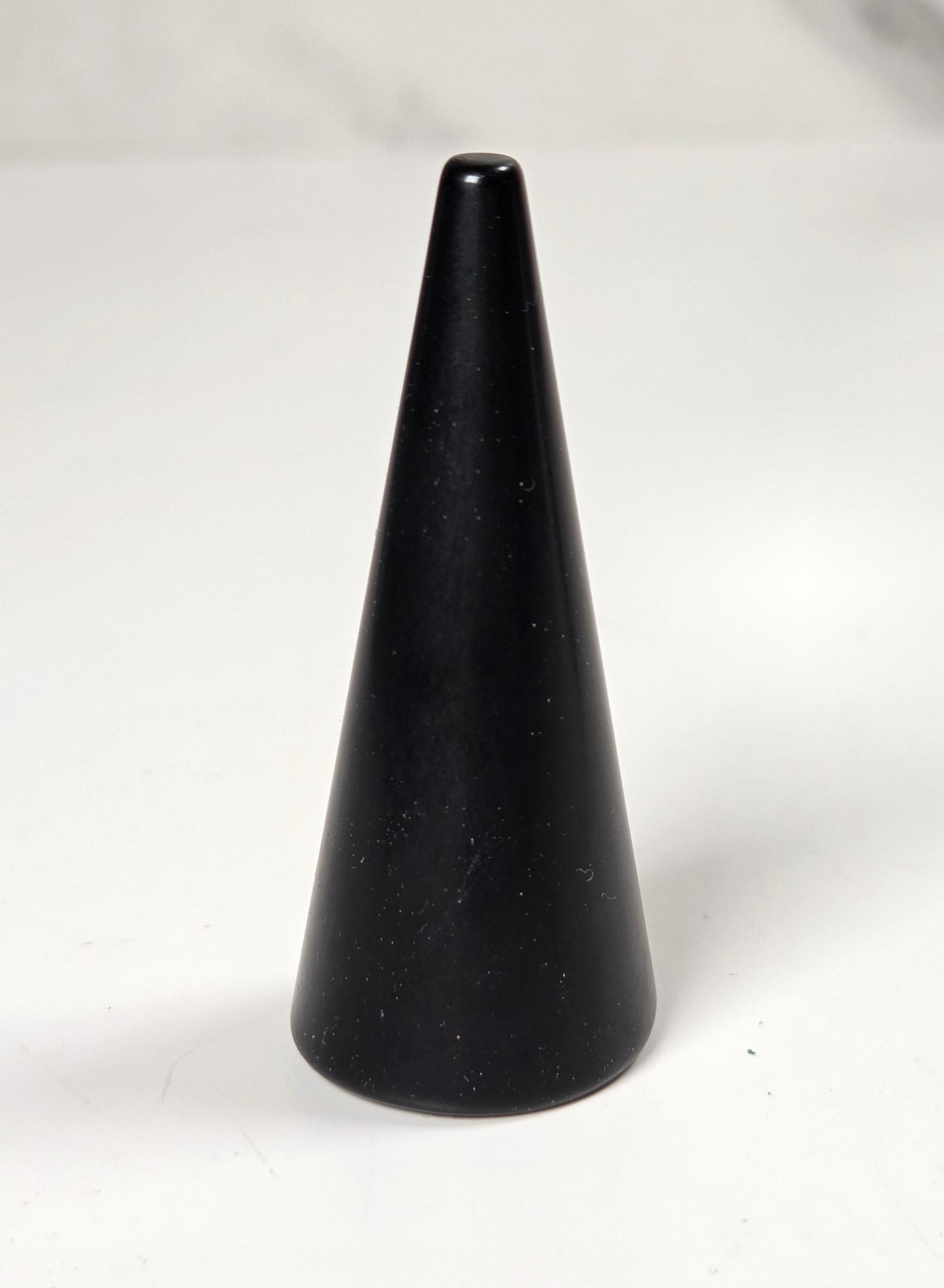 A small black cone-shaped object, possibly a candle holder or decorative object, standing on a white surface with a blurred gray background.