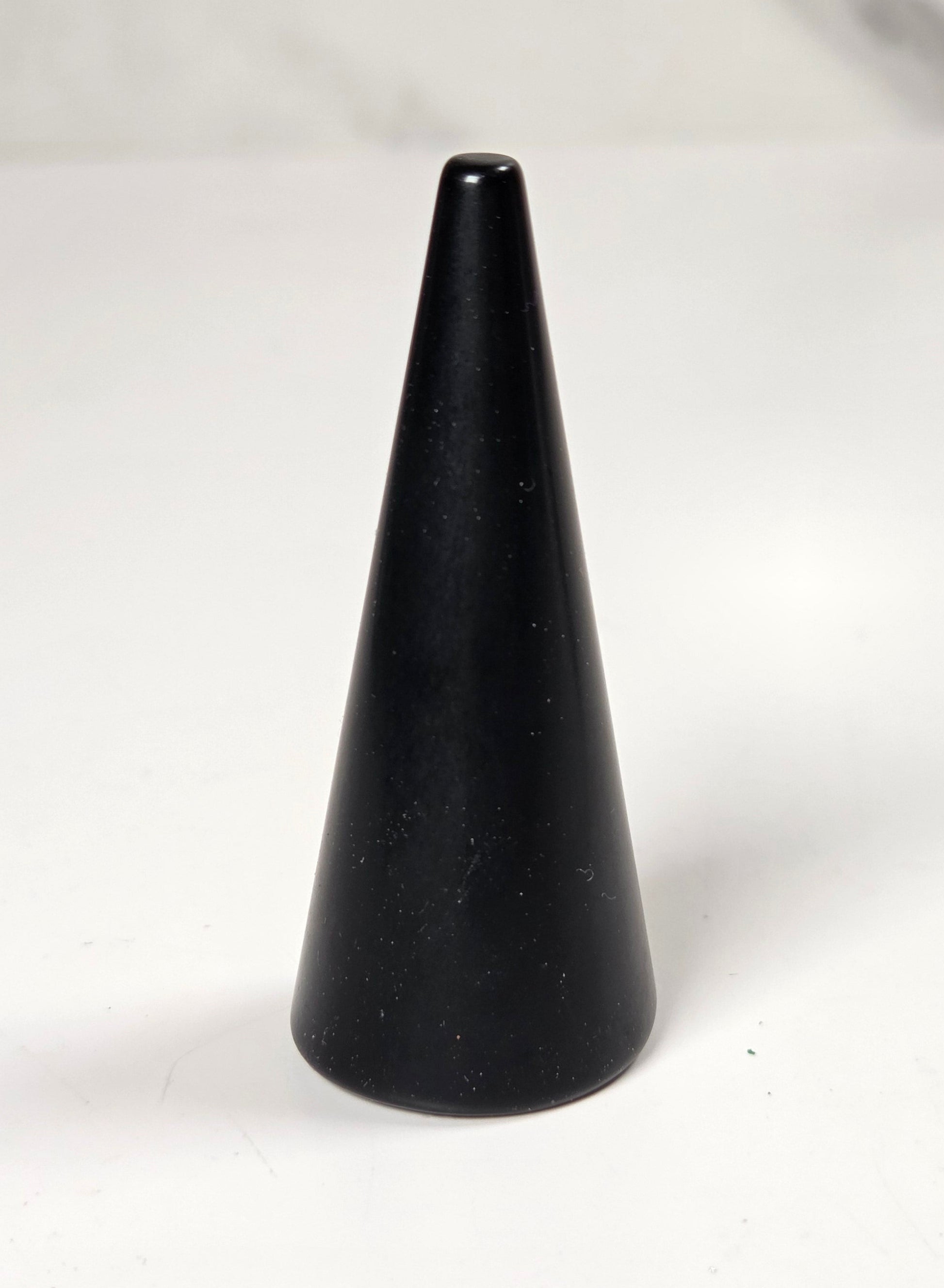 A small black cone-shaped object, possibly a candle holder or decorative object, standing on a white surface with a blurred gray background.