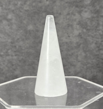 A frosted white cone-shaped object displayed upright on a clear hexagonal acrylic stand against a textured gray background.