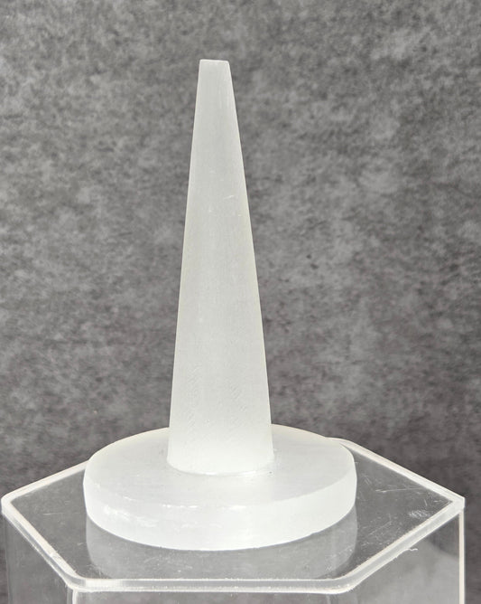 A frosted white silicone applicator tip mounted on a clear acrylic hexagonal stand, set against a textured gray background.