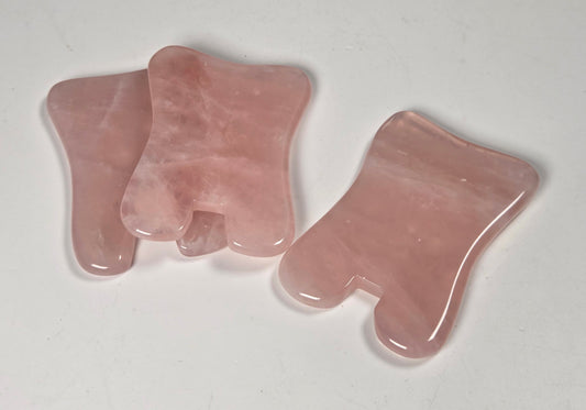 Three pink rose quartz gua sha massage tools arranged on a plain white surface.