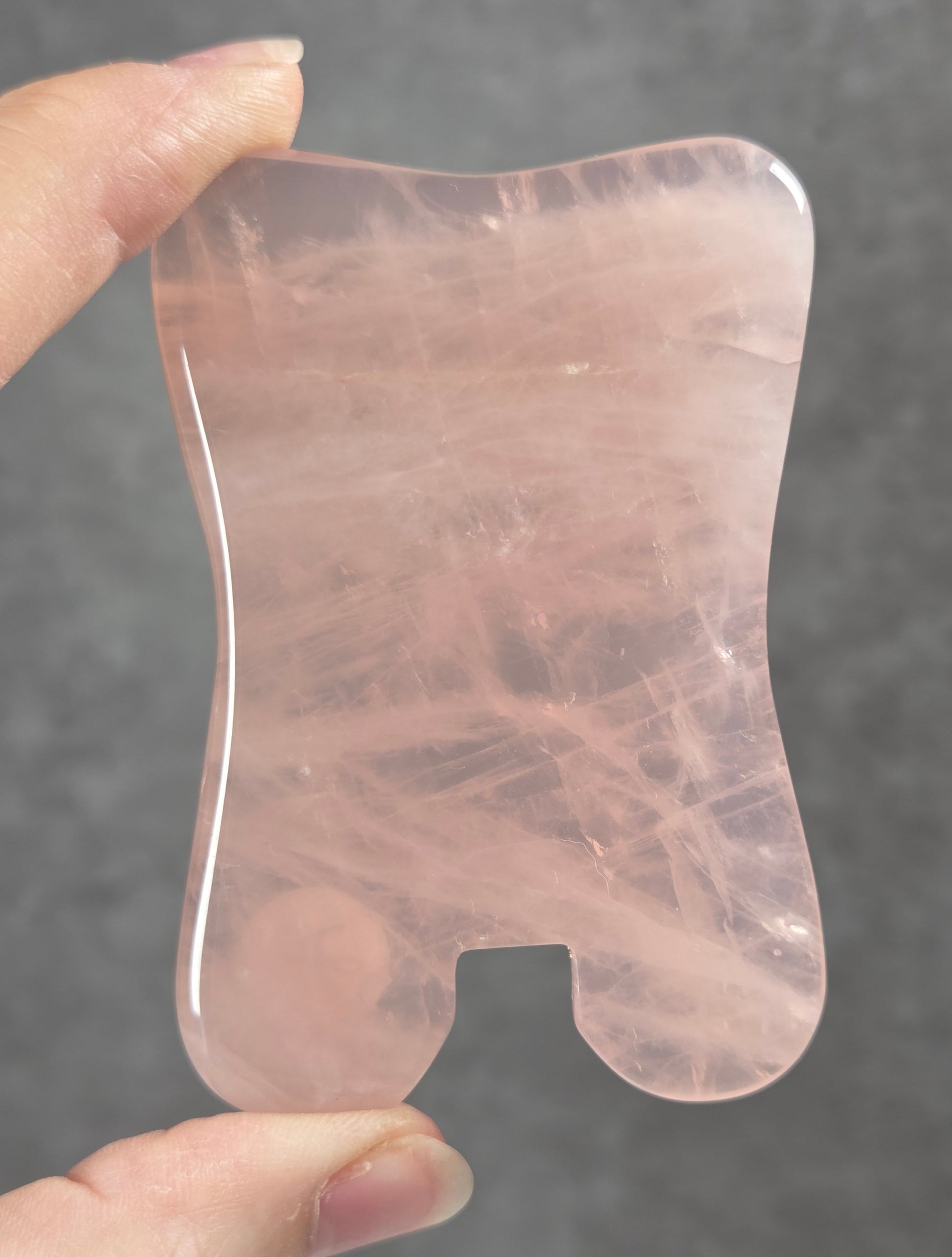  Hand holding a pink rose quartz gua sha massage tool against a plain black surface.