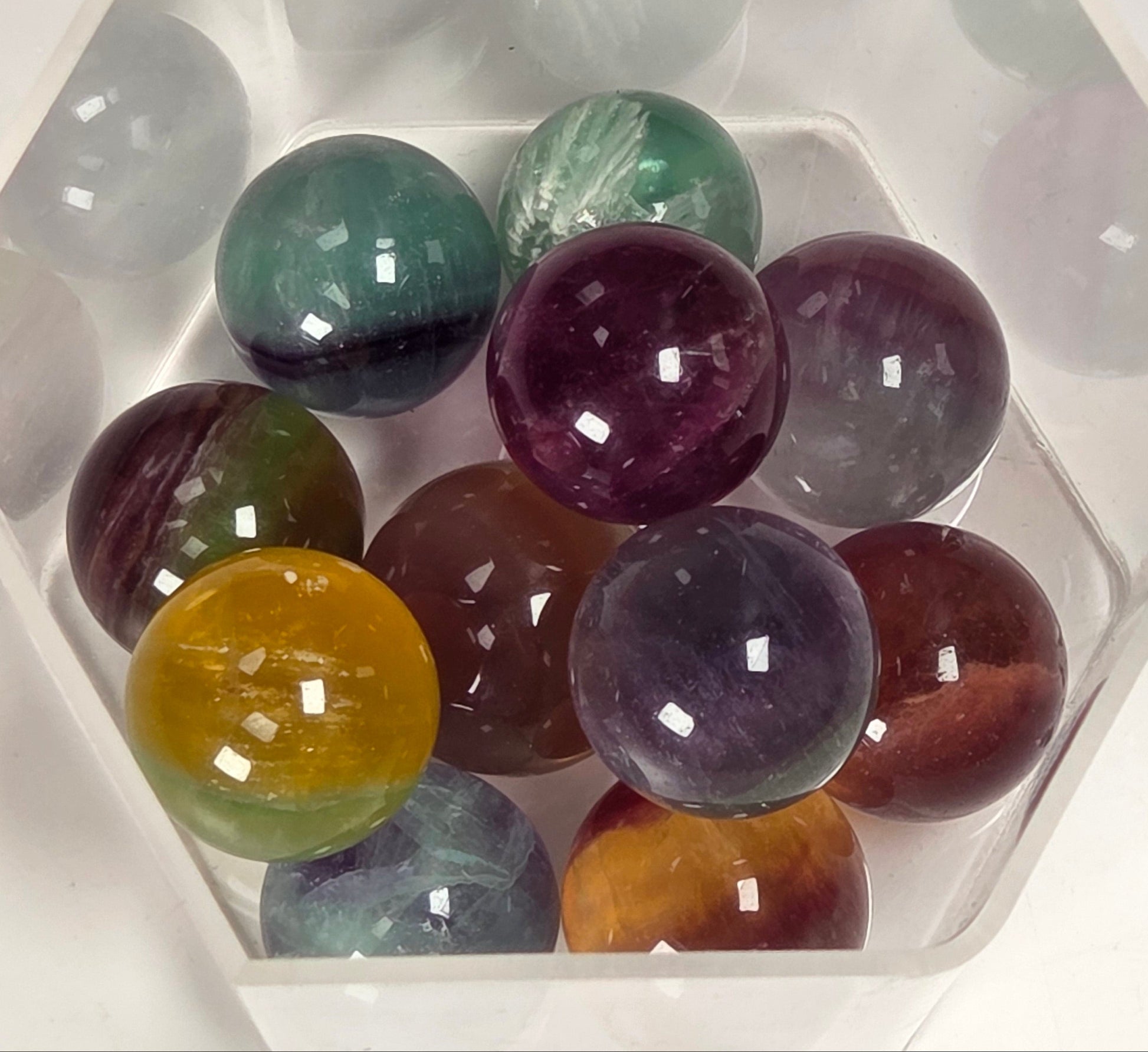 A set of polished multicolor crystal balls arranged inside a clear hexagonal plastic container on a white background.