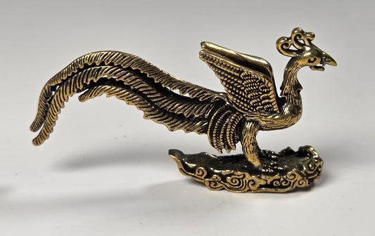 An antique-style metallic phoenix figurine with a long curved tail, detailed feather textures, and a cloud-like base, shown on a neutral light gray background.