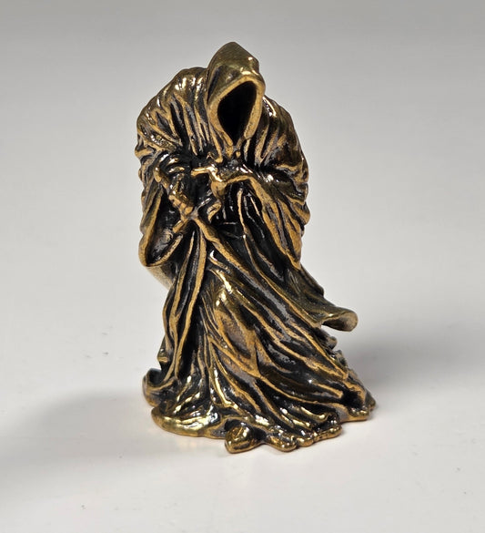 A small bronze figurine of a hooded, faceless robed figure standing on a plain light gray surface.