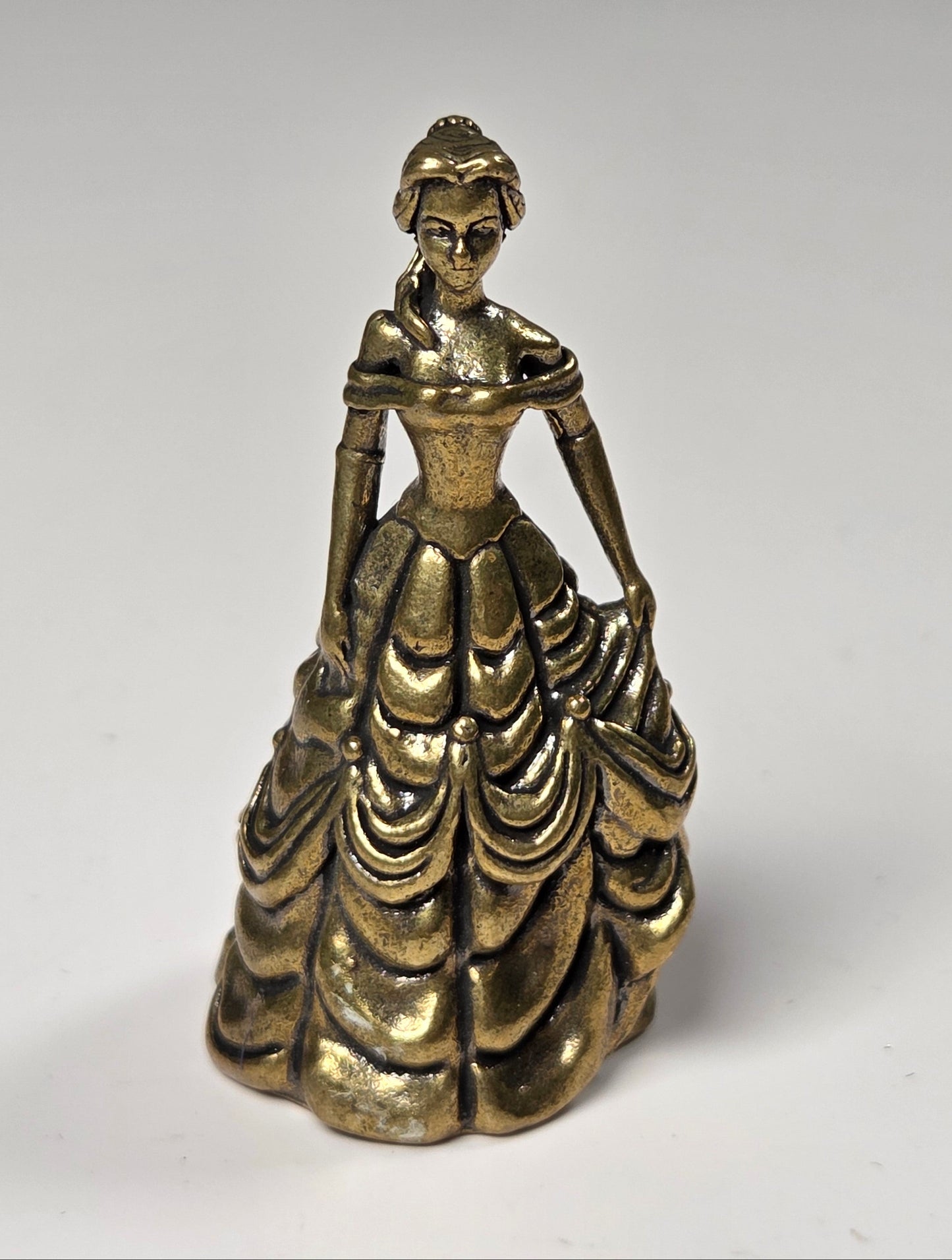 A small metallic figurine of a woman in an ornate, tiered ball gown, photographed against a plain light gray background.