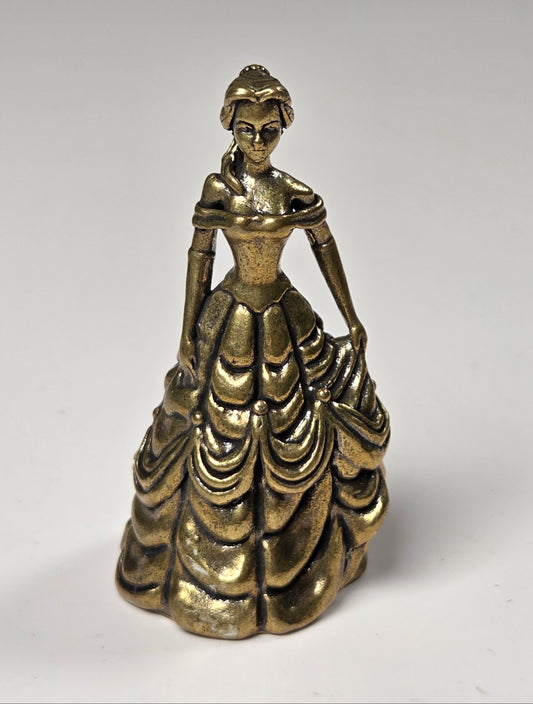A small metallic figurine of a woman in an ornate, tiered ball gown, photographed against a plain light gray background.