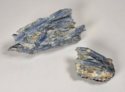 Two rough blue-gray mineral specimens with crystalline texture on a plain light background.