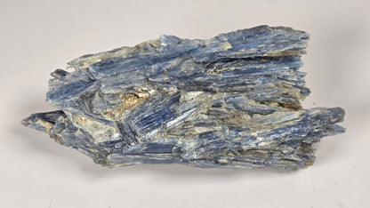A natural blue specimenwith layered, flaky crystalline structure, photographed on a plain light gray background.